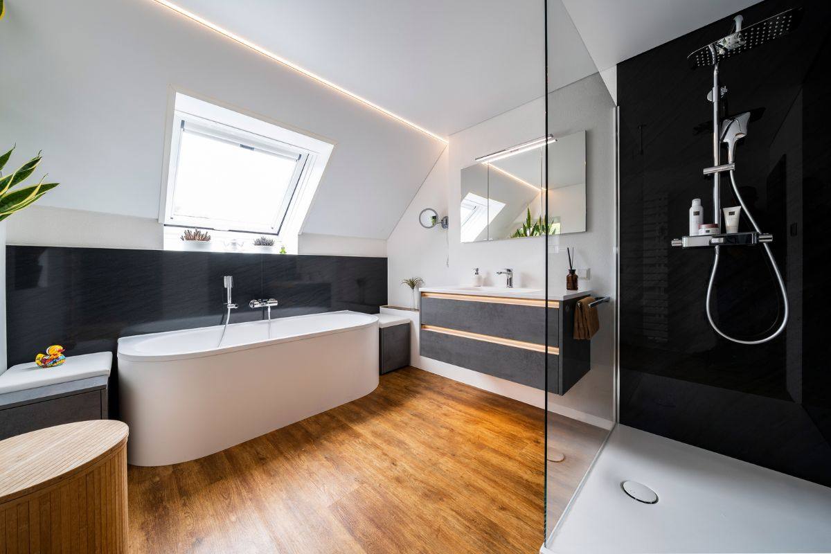 Wohlfühlbad unter der Dachschräge mit frei stehender Badewanne, Holzboden und Dusche mit dunkler Wand