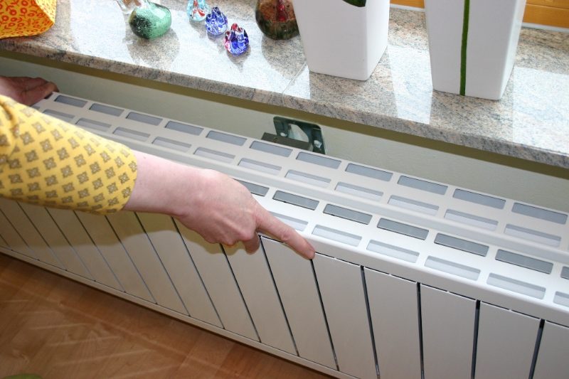 Eine Hand klappt einen Heizkörper unter der Fensterbank nach vorn